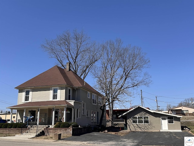 view of front facade with a porch, a chimney, and aphalt driveway