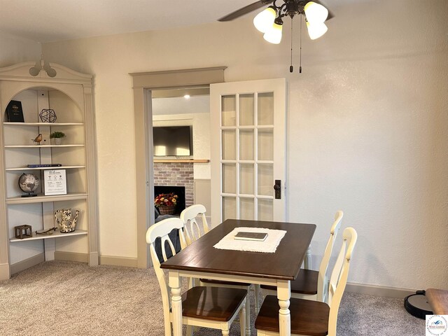 dining area with a fireplace, light colored carpet, baseboards, and a ceiling fan