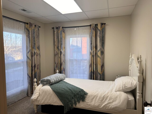 carpeted bedroom featuring multiple windows, a paneled ceiling, and visible vents