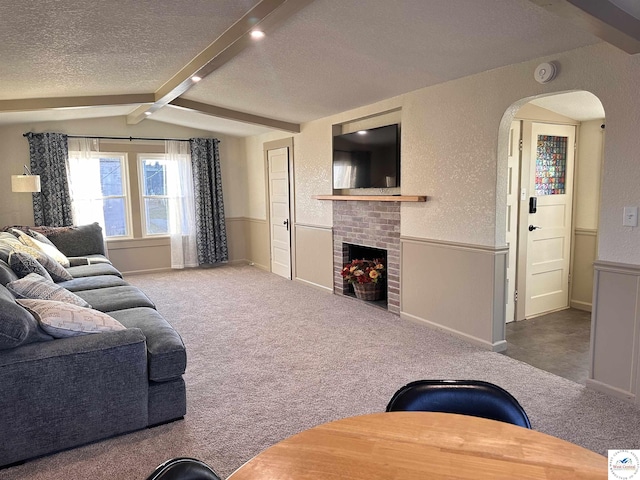 carpeted living area featuring wainscoting, a brick fireplace, a textured ceiling, and lofted ceiling with beams