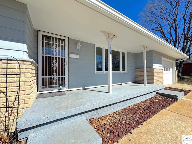 view of exterior entry featuring a garage, brick siding, and a porch