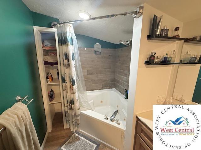 bathroom featuring a textured ceiling, wood finished floors, a combined bath / shower with jetted tub, and vaulted ceiling