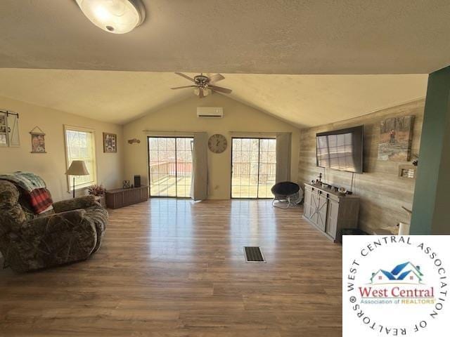 living room featuring a ceiling fan, vaulted ceiling, wood finished floors, and a wall mounted AC