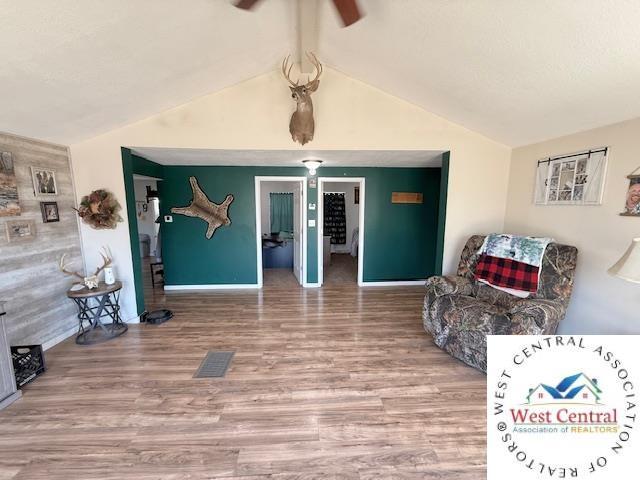 living room featuring visible vents, baseboards, lofted ceiling, and wood finished floors