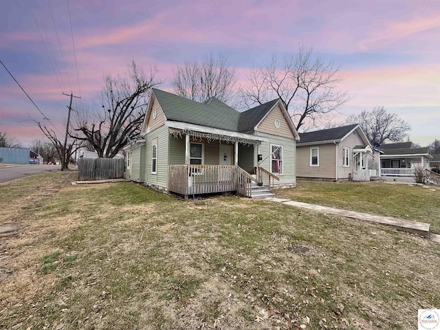 bungalow-style home featuring roof with shingles, fence, and a yard