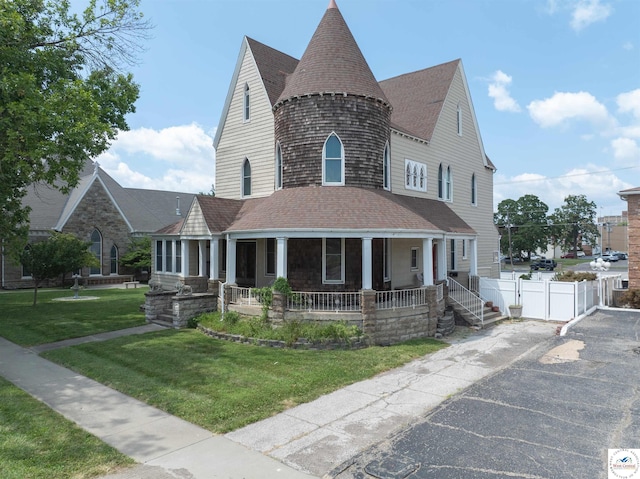 view of front facade with a porch, a front yard, fence, and a shingled roof