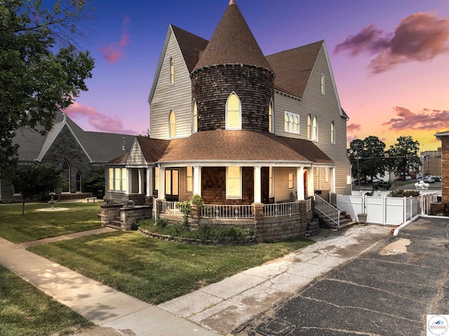 view of front of property with a porch, a yard, a shingled roof, and fence