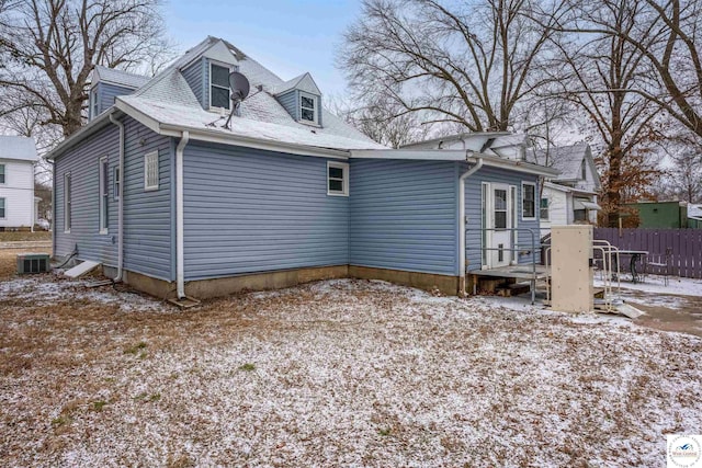 snow covered back of property featuring central AC unit and fence