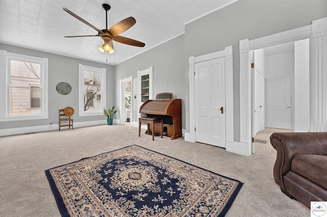 living area featuring a ceiling fan, carpet, ornamental molding, and baseboards