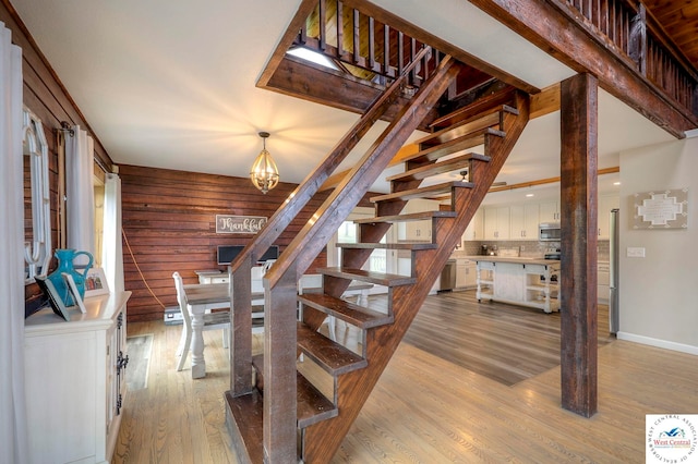 stairs featuring baseboards, wood walls, wood finished floors, and a notable chandelier