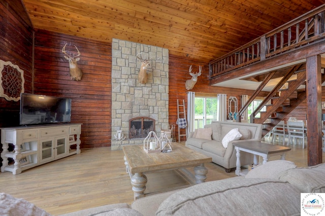 living room featuring high vaulted ceiling, a fireplace, wood ceiling, stairs, and light wood finished floors