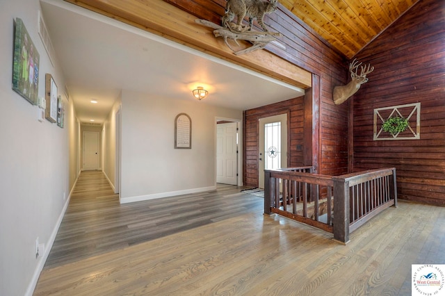 hallway with an upstairs landing, lofted ceiling, baseboards, and wood finished floors