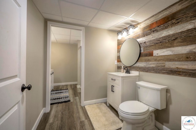 half bathroom featuring baseboards, toilet, wood finished floors, vanity, and a paneled ceiling