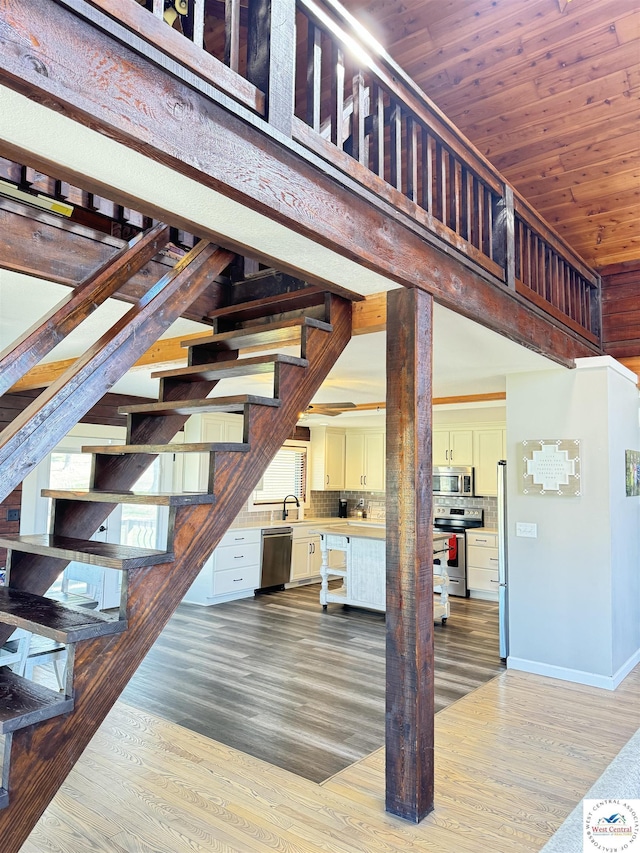 staircase featuring wood ceiling, a towering ceiling, baseboards, and wood finished floors