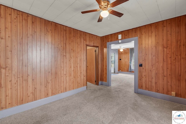 empty room with ceiling fan, carpet floors, baseboards, and wooden walls