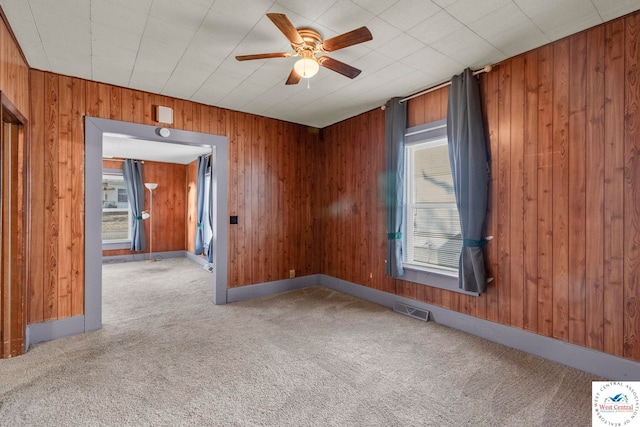 carpeted spare room with wood walls, plenty of natural light, visible vents, and a ceiling fan