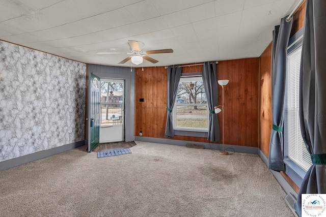 interior space featuring wooden walls, baseboards, visible vents, a ceiling fan, and carpet flooring