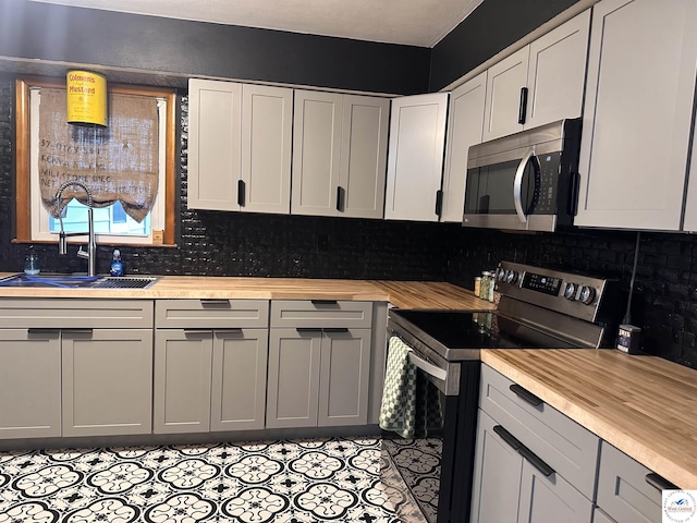 kitchen with appliances with stainless steel finishes, backsplash, light tile patterned flooring, and butcher block counters