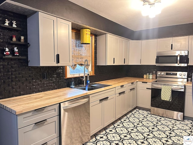 kitchen with stainless steel appliances, a sink, wood counters, and tasteful backsplash