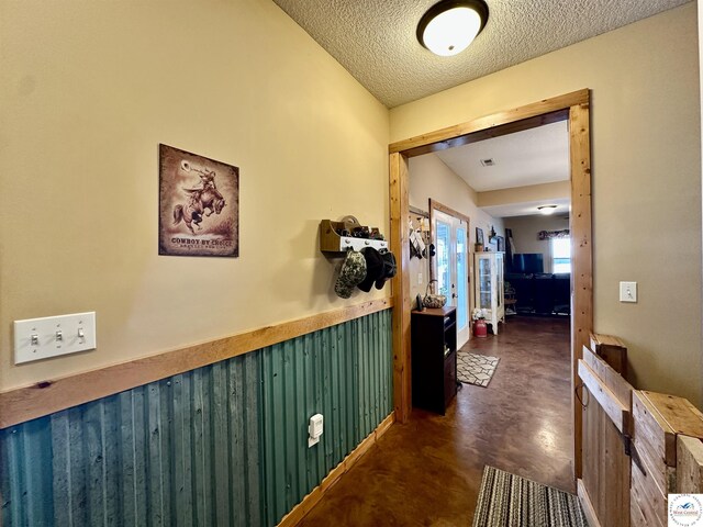 hallway with a textured ceiling, concrete flooring, and wainscoting