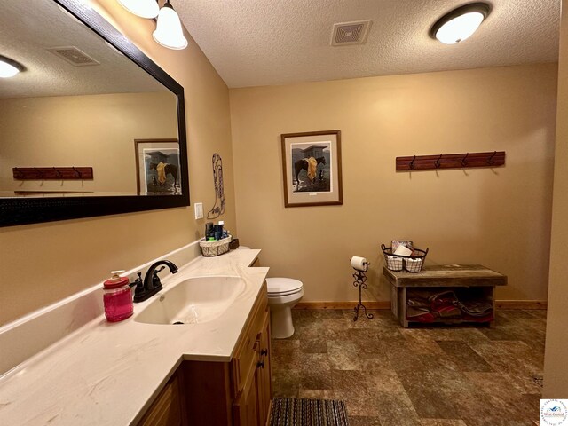 bathroom featuring toilet, a textured ceiling, vanity, and visible vents