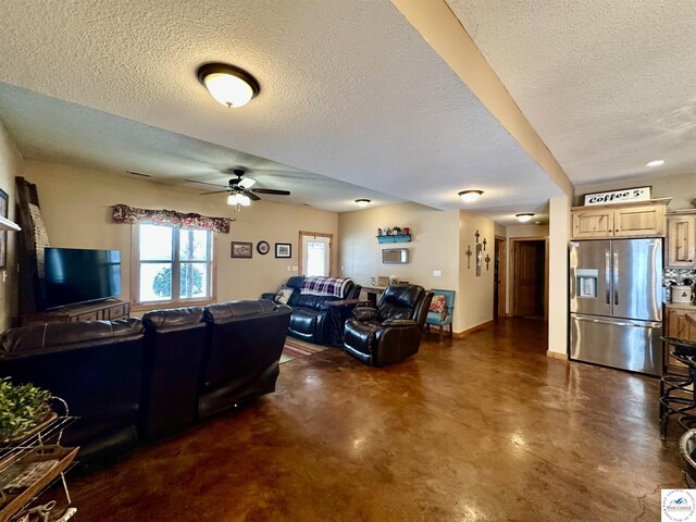 living room with ceiling fan, finished concrete floors, baseboards, and a textured ceiling