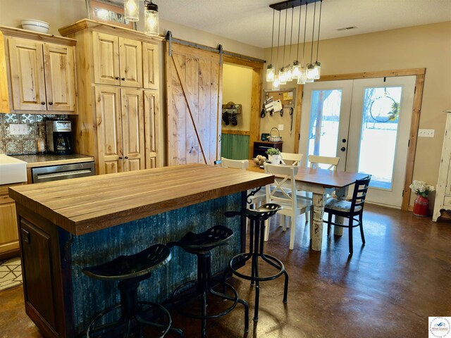 kitchen featuring a barn door, decorative backsplash, butcher block counters, concrete flooring, and french doors