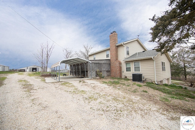 back of house featuring central AC, roof with shingles, a chimney, and a detached carport