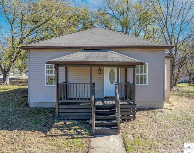 bungalow featuring a porch, a front yard, and roof with shingles