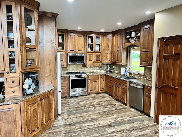 kitchen with stone counters, stainless steel appliances, a sink, dark wood finished floors, and glass insert cabinets