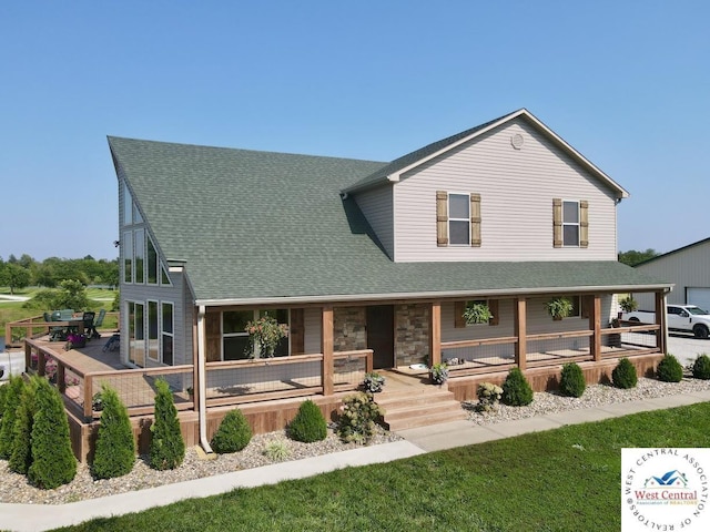 farmhouse-style home featuring a shingled roof, covered porch, and stone siding