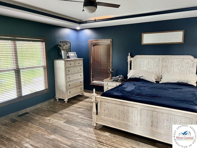 bedroom with a raised ceiling, visible vents, a ceiling fan, wood finished floors, and baseboards