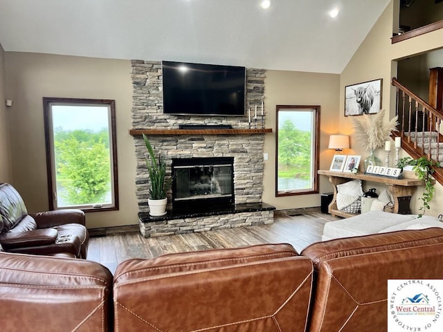 living area with stairway, vaulted ceiling, a stone fireplace, and wood finished floors