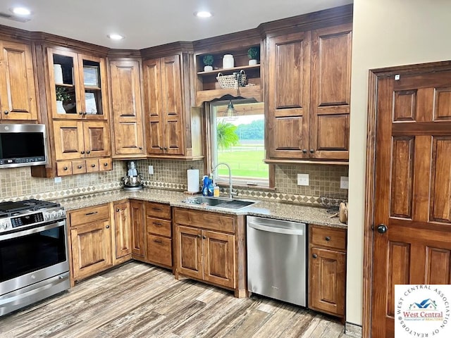 kitchen featuring light stone counters, open shelves, appliances with stainless steel finishes, a sink, and light wood-type flooring