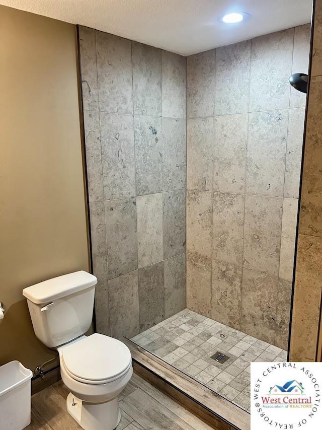 bathroom with toilet, a shower stall, a textured ceiling, and wood finished floors