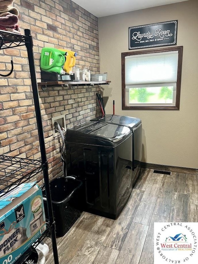 laundry room with brick wall, wood finished floors, washer and dryer, laundry area, and baseboards