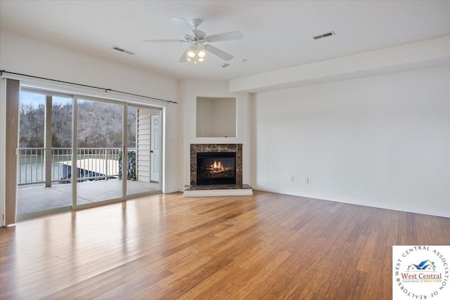 unfurnished living room with a premium fireplace, visible vents, light wood-style flooring, and a ceiling fan