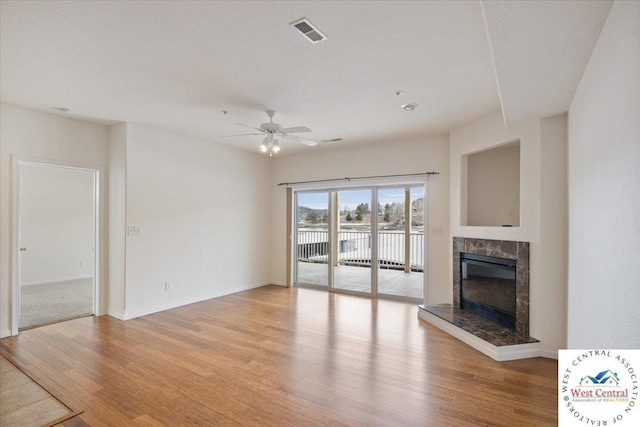 unfurnished living room featuring a high end fireplace, visible vents, baseboards, light wood-style flooring, and a ceiling fan