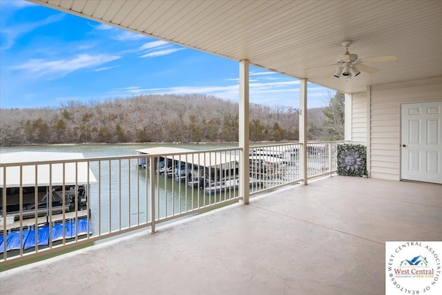 view of patio with a balcony, a wooded view, a ceiling fan, and a water view