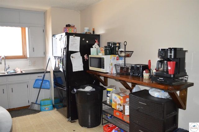 kitchen featuring white microwave, light floors, freestanding refrigerator, a sink, and dark countertops