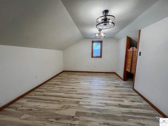 bonus room featuring lofted ceiling, a textured ceiling, wood finished floors, and baseboards