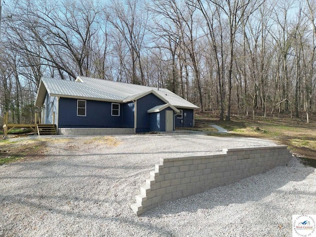 view of side of home featuring gravel driveway and metal roof