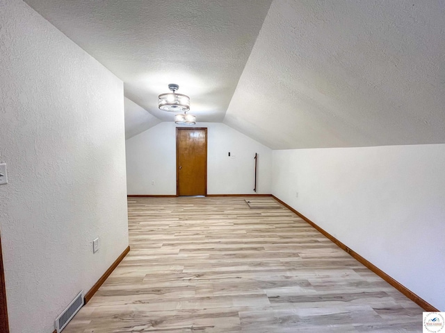 additional living space with a textured ceiling, visible vents, light wood-type flooring, and baseboards