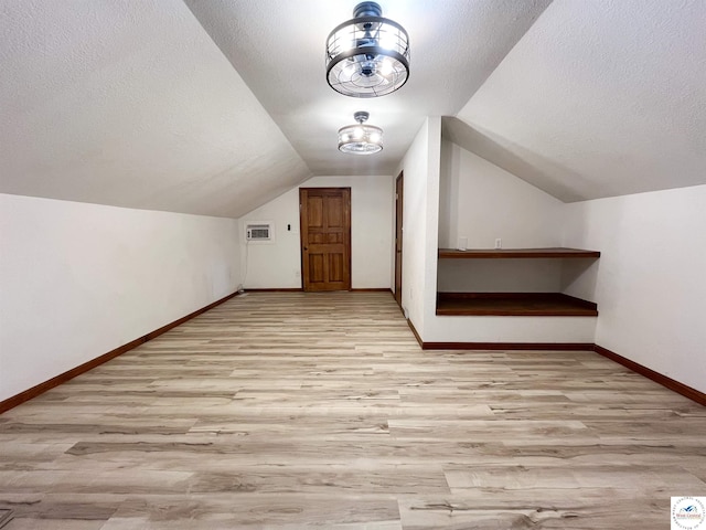 additional living space featuring baseboards, a textured ceiling, and light wood finished floors