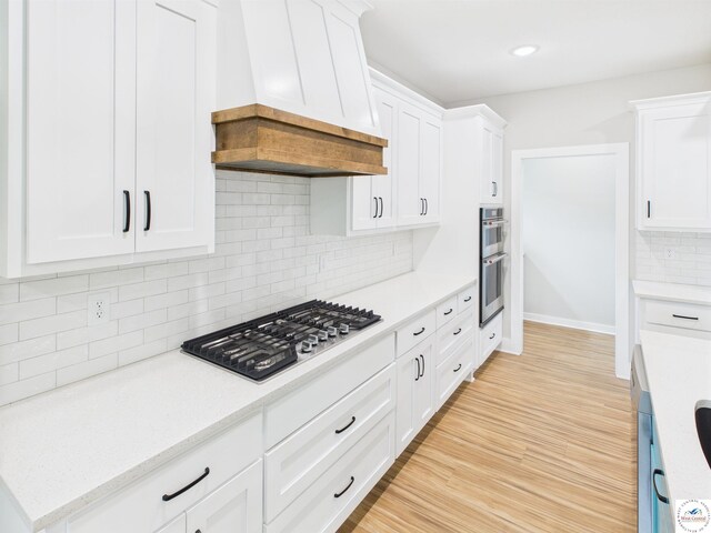 1248 Rich Blvd, Warrensburg, MO 64093 - kitchen featuring appliances with stainless steel finishes, custom exhaust hood, white cabinetry, backsplash, and light wood-style floors