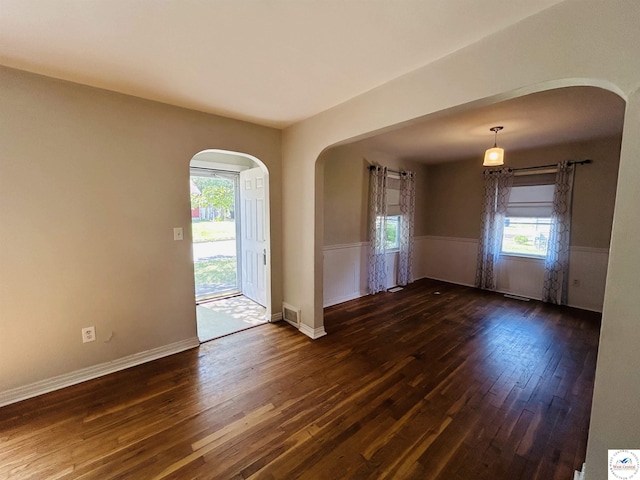 607 Laurel St, Warrensburg, MO 64093 - spare room featuring arched walkways, dark wood-type flooring, and a wainscoted wall