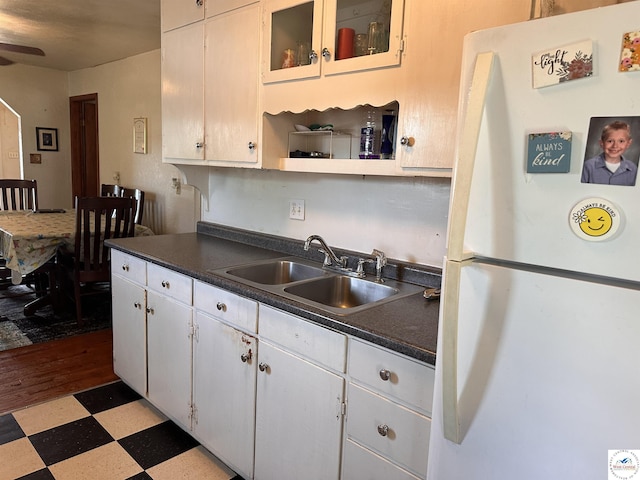 kitchen featuring freestanding refrigerator, a sink, dark countertops, light floors, and white cabinetry
