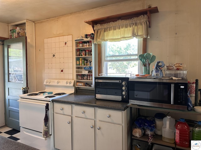 kitchen featuring electric range, stainless steel microwave, white cabinets, light flooring, and dark countertops