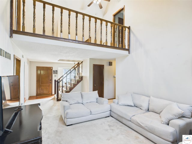 living area with stairway, a ceiling fan, carpet, and a high ceiling