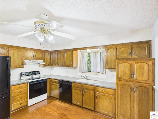 kitchen with black appliances, under cabinet range hood, a sink, light wood finished floors, and brown cabinetry